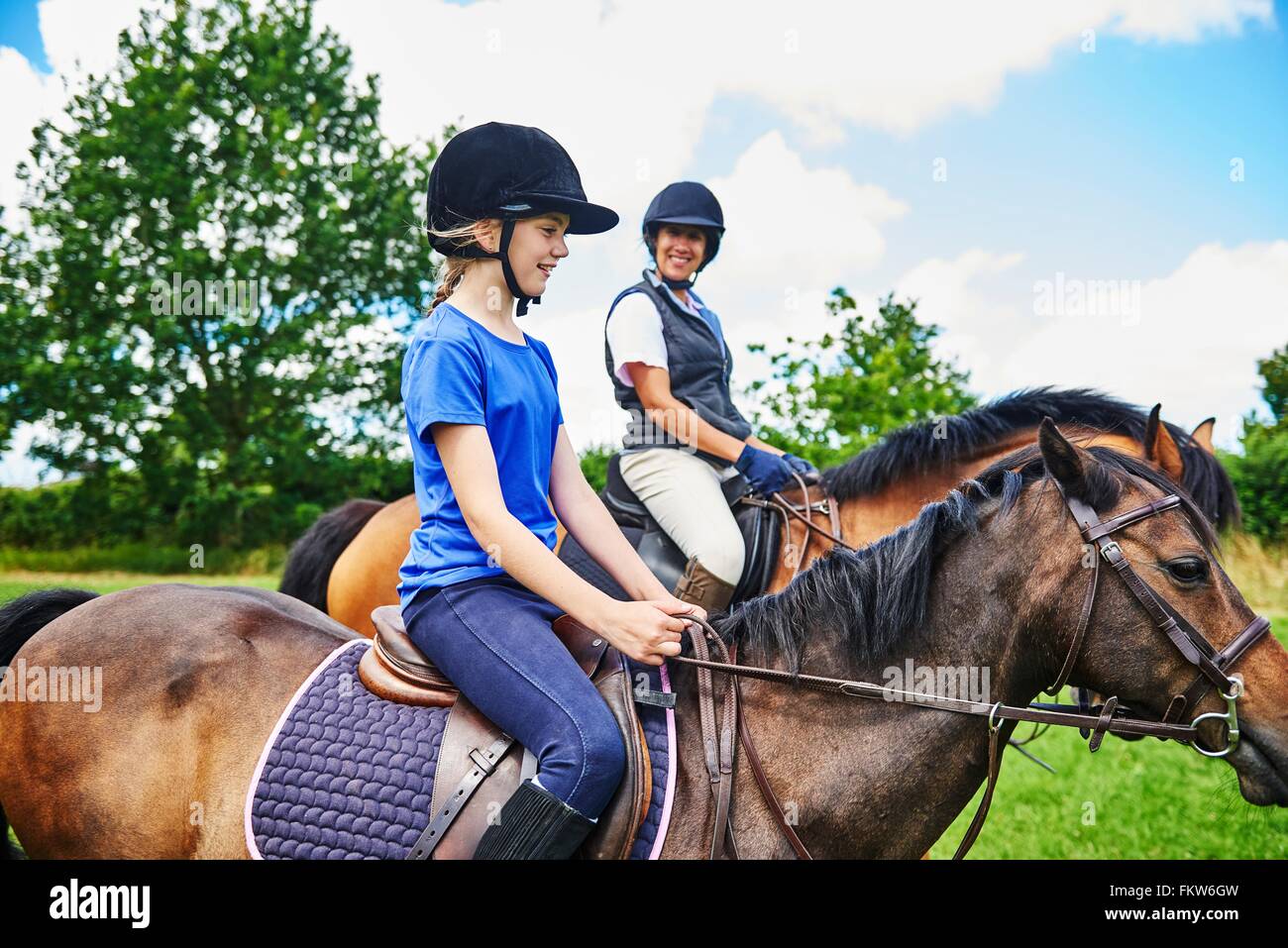 Vista lateral de la mujer madura y chica a caballo vistiendo gorras de equitación sonriendo Foto de stock