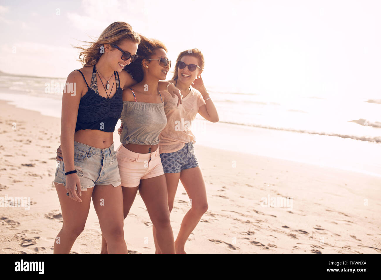 Retrato de tres amigas jóvenes caminando por la orilla del mar. Las mujeres jóvenes multirracial paseando por la playa en un día de verano Foto de stock