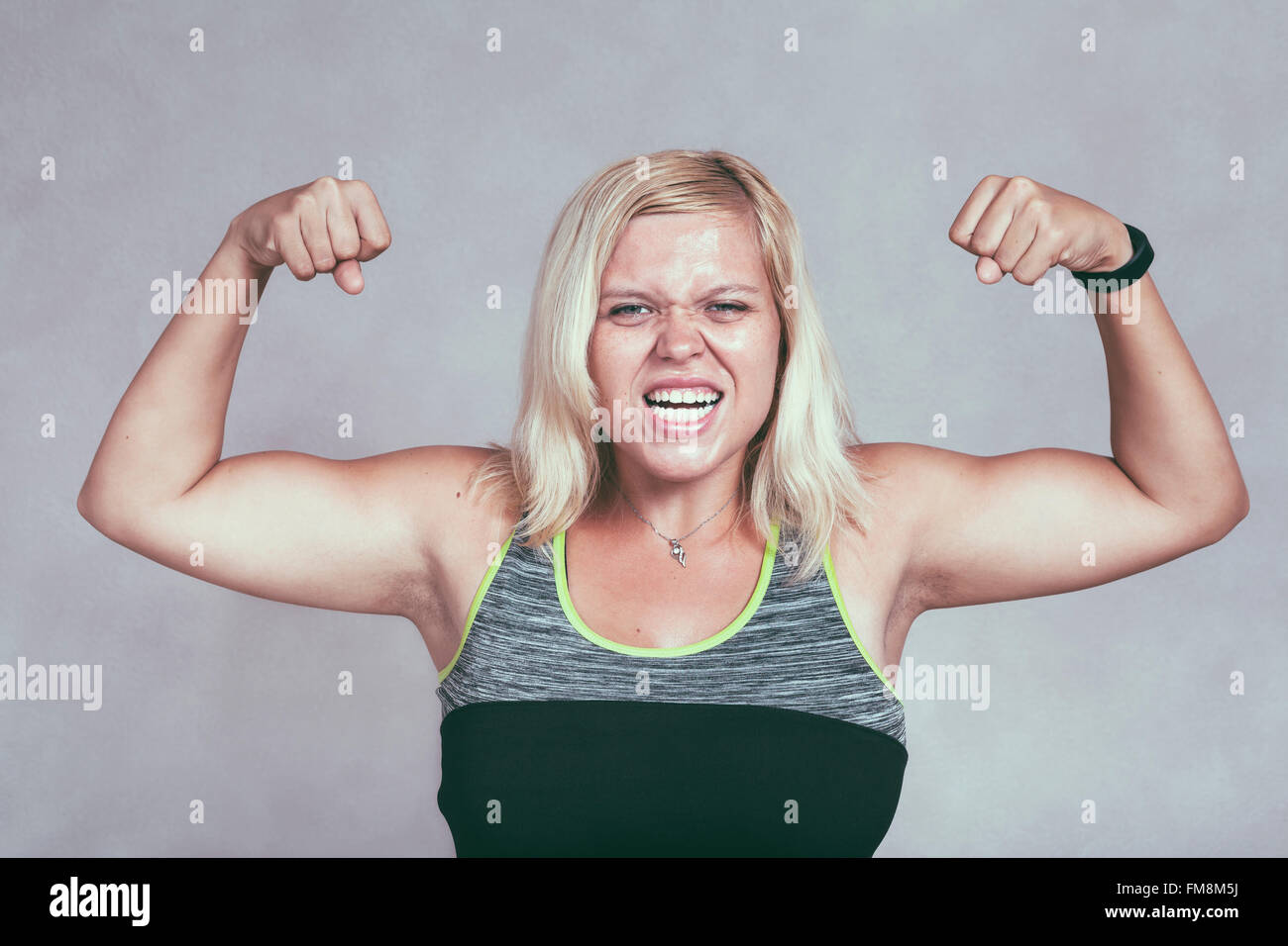 Fuerte muscular Emocionados mujer flexionando sus músculos. Joven rubia femenina deportiva mostrando brazos y bíceps. Foto de stock