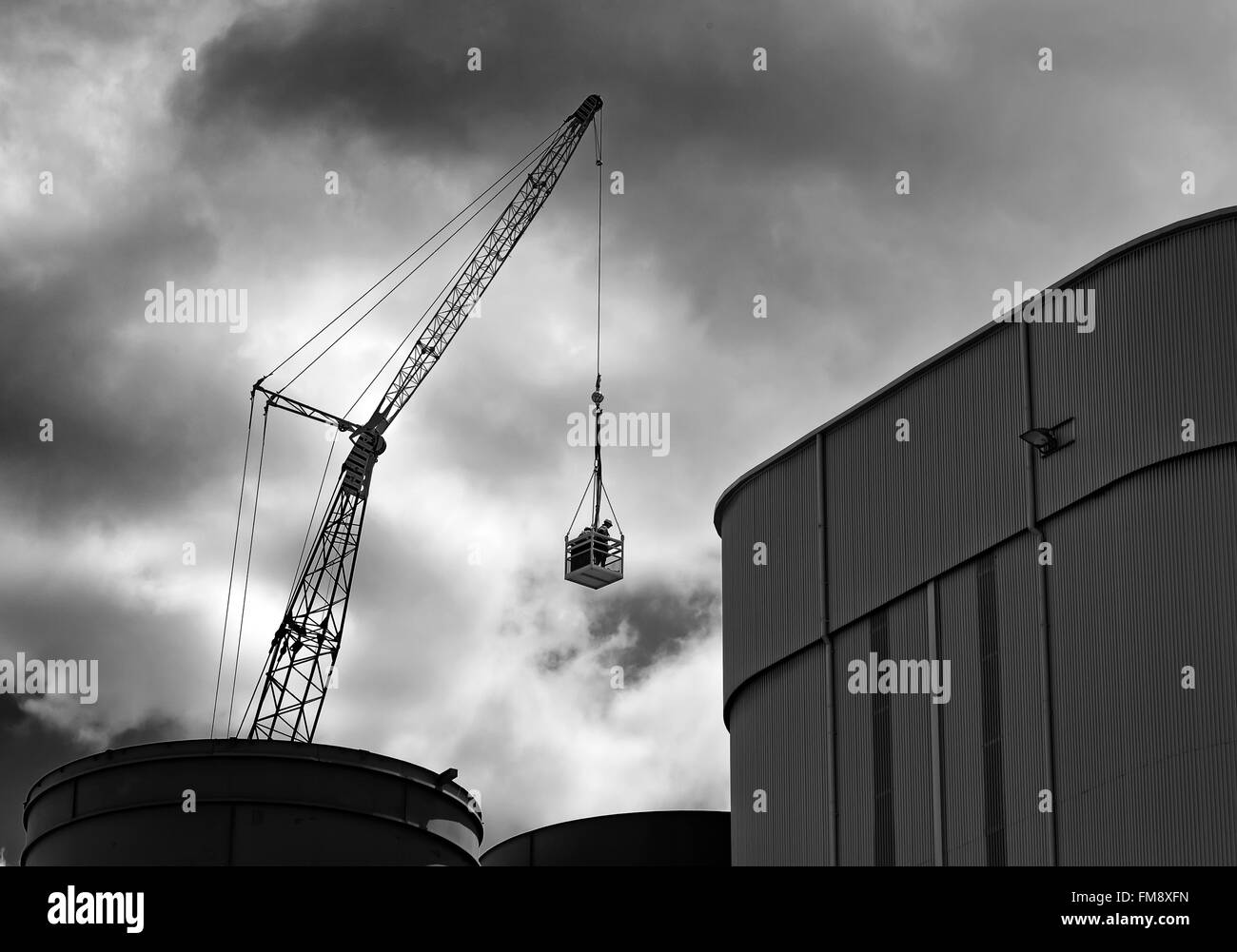 Escena industrial del hombre en el canasto bajo el cielo oscuro izada por la grúa en un silo en Brisbane docks Foto de stock