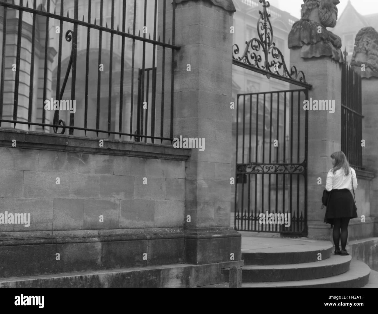 Un estudiante vestido con camisa blanca y tradicional falda negra, espera fuera del Teatro Sheldonian, Oxford, Reino Unido. Blanco y negro. Foto de stock