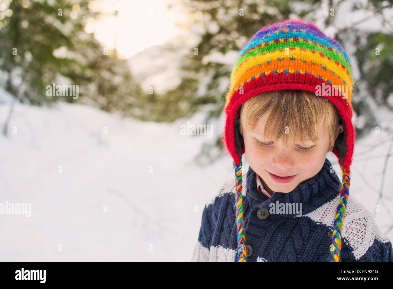 Chico en sombrero multicolor en la nieve mirando hacia abajo Foto de stock
