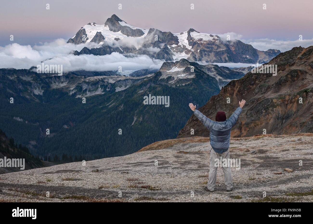 Hombre de pie con los brazos levantados, Mount Shuksan, Washington, Estados Unidos Foto de stock