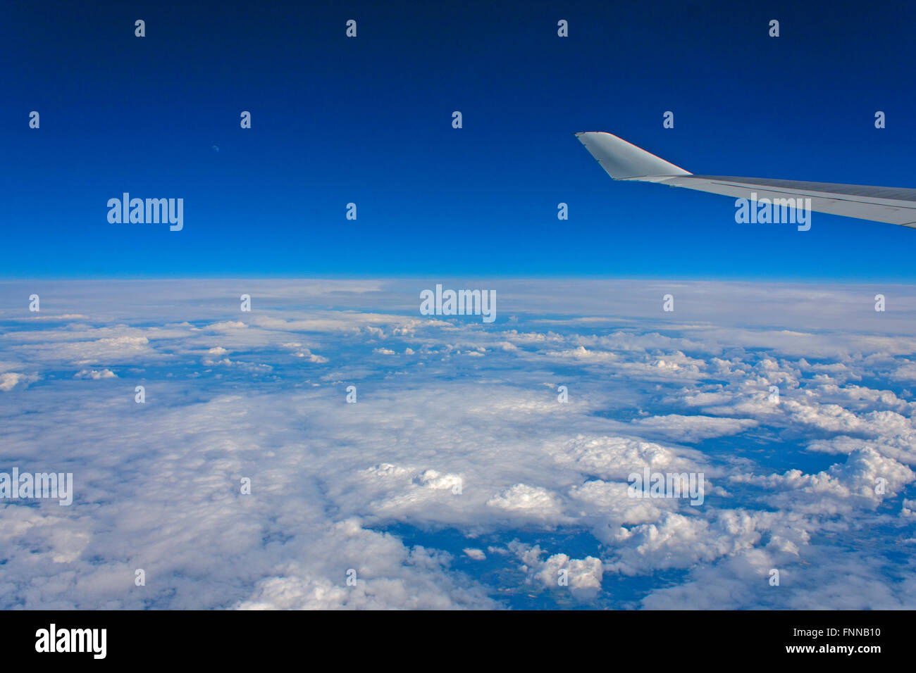 Vista desde la ventana de un avión por encima de las nubes mirando hacia abajo en Holanda con la Luna visible en el cielo azul por encima Foto de stock