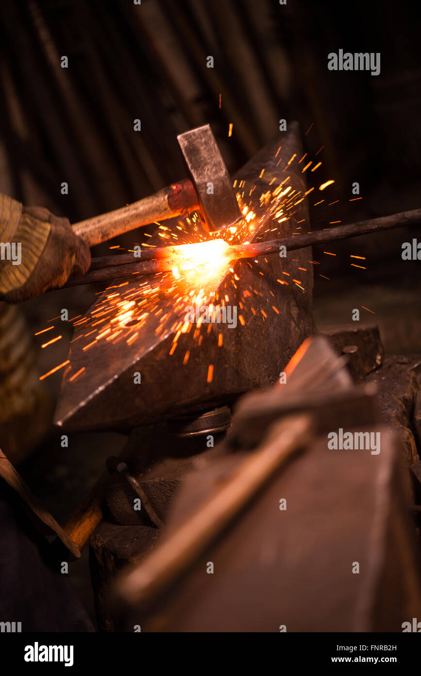 Herrero conformando un pedazo de hierro caliente sobre un yunque con un  martillo, con chispas de volar Fotografía de stock - Alamy
