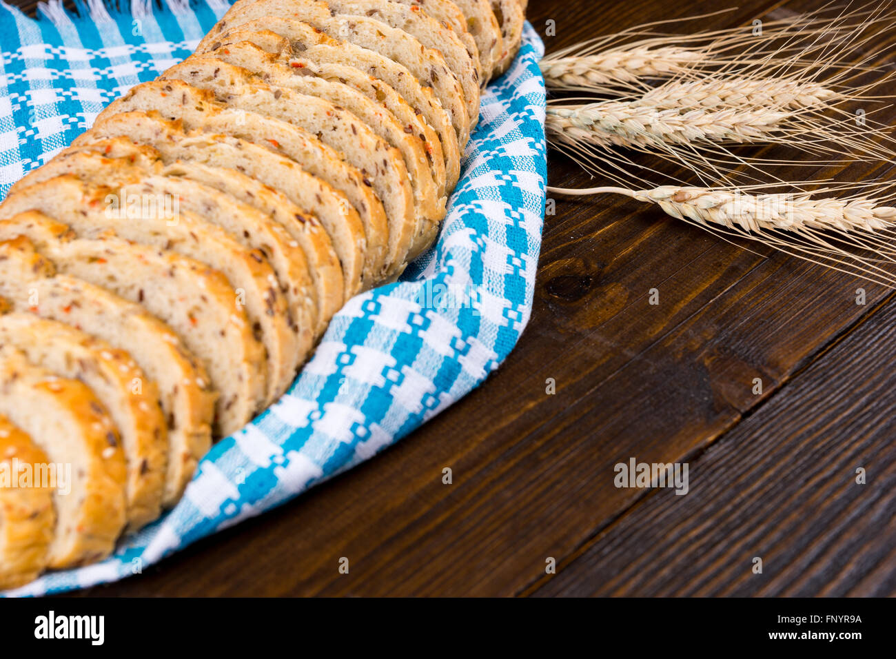 Rodajas de pan integrales sanos muestran en una servilleta azul y blanco de estilo rústico con tres espigas de trigo de oro madura sobre una tabla de madera con espacio de copia. Foto de stock