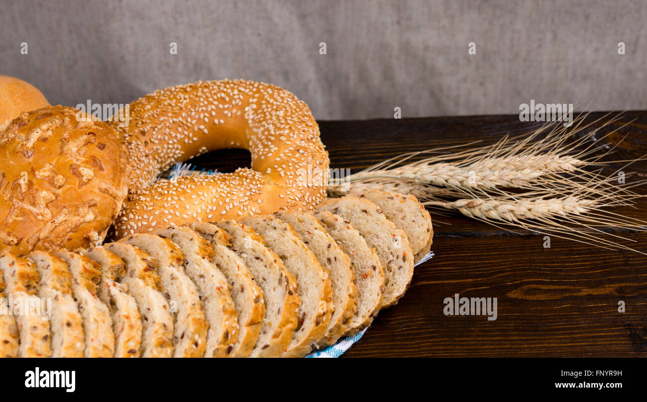 Surtido de panes sembrados en una tabla rústica con rodajas de pan integrales, un bagel de sésamo y queso bun con espigas de trigo maduro junto a copiar y el espacio. Foto de stock