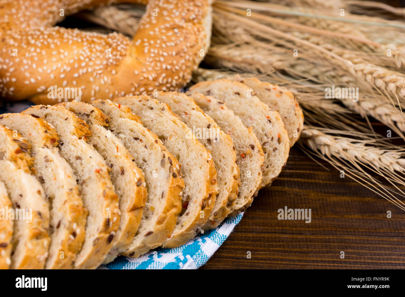 Rodajas de pan integrales con sésamo bagel aparece en una servilleta azul y blanco con espigas de trigo maduro, Vista cercana Foto de stock