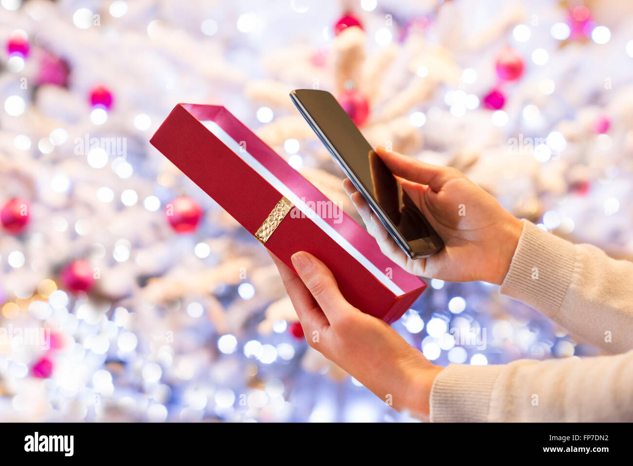 Mujer descubre un smartphone en regalo de Navidad. Boke antecedentes del árbol de navidad Foto de stock