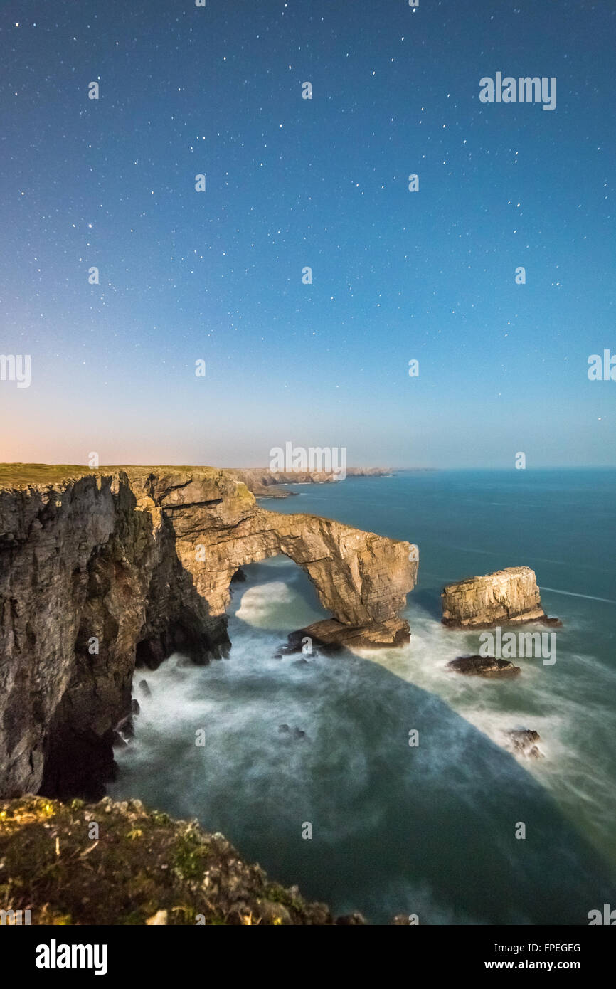 Cerca de una luna llena ilumina el Puente Verde de Gales y el sur de la costa de Pembrokeshire Foto de stock