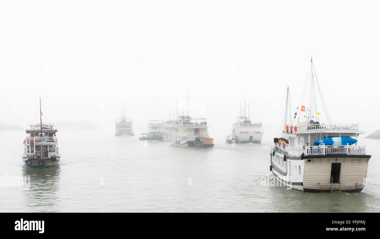 La Bahía de Halong, Vietnam Una flotilla de buques de crucero turísticos dirigirse hacia el vaho en un día húmedo en enero. Foto de stock