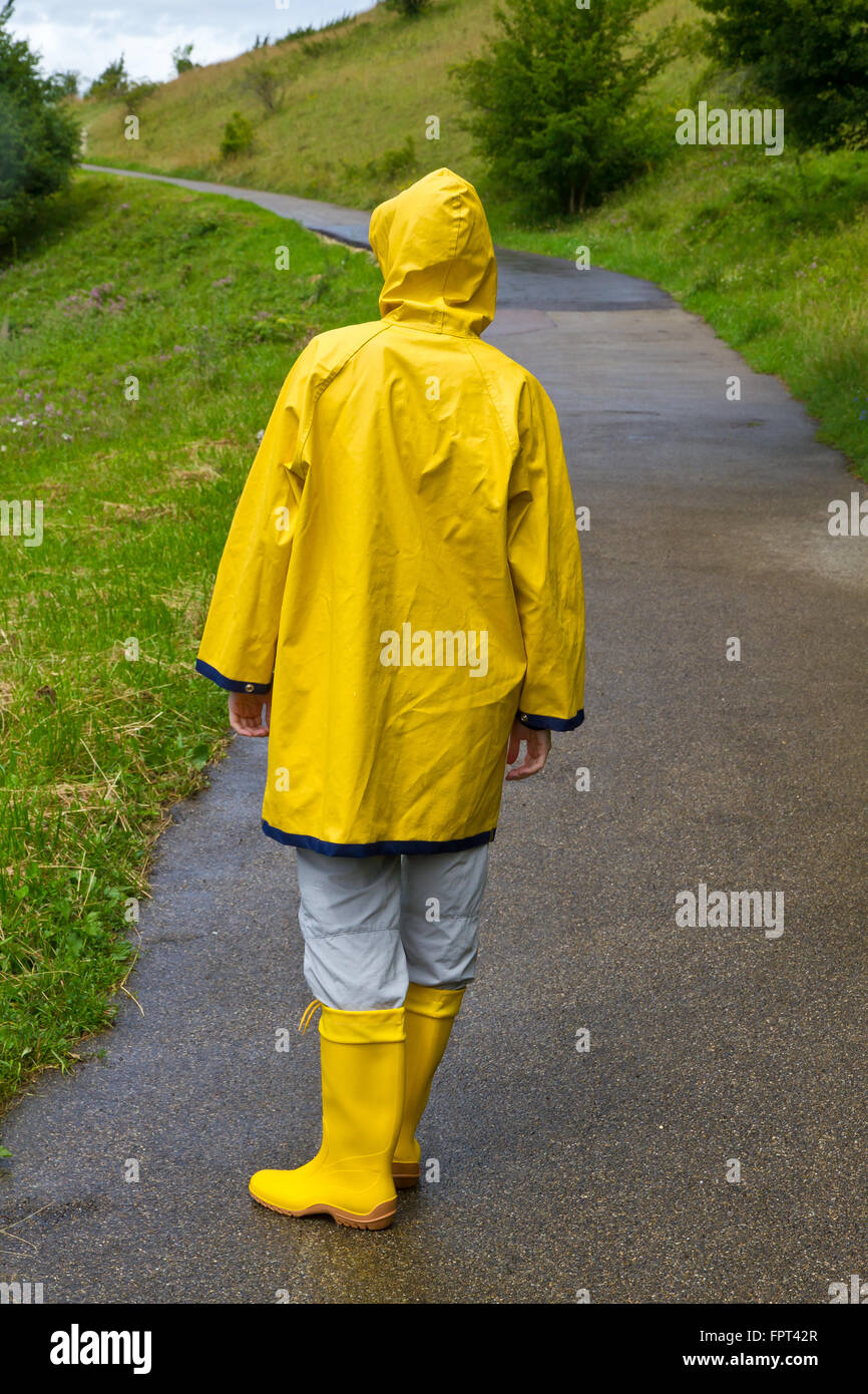 tos mineral lector Mujer joven vistiendo un amarillo impermeable y botas de goma de caminar en  la naturaleza Fotografía de stock - Alamy