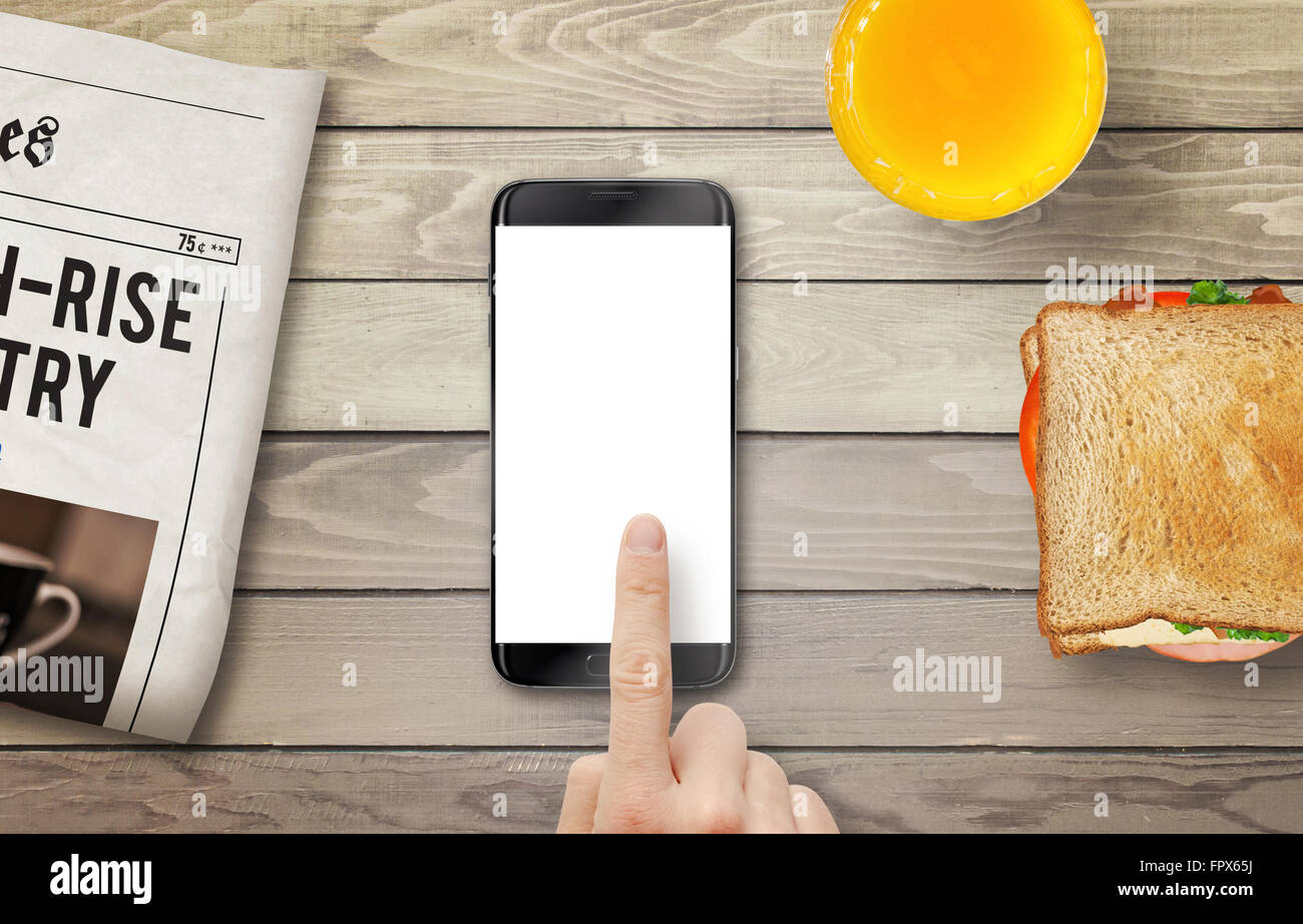 Teléfono inteligente con pantalla aislado para el boceto. La mano tocando la pantalla. Periódico, jugo y un sándwich en la tabla. Vista desde arriba. Foto de stock