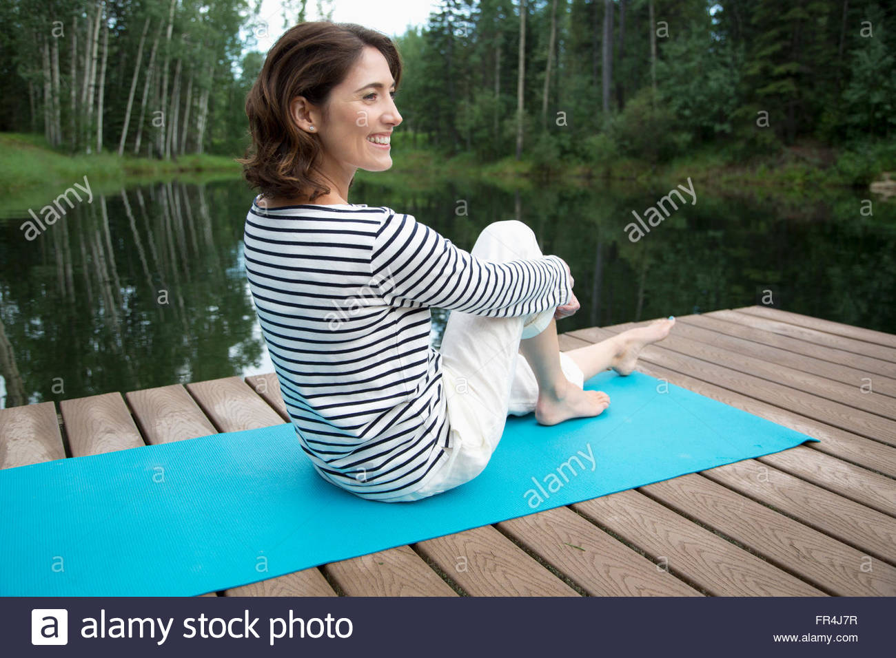 Bonita, mujer de mediana edad relajante en la estera del yoga en boat dock Foto de stock