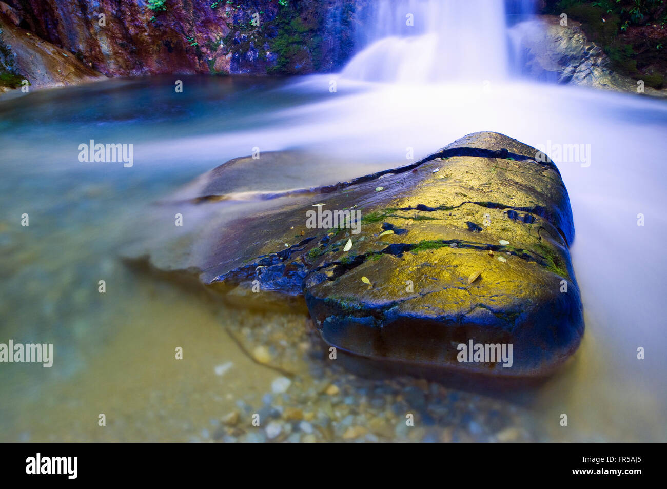 Una imagen horizontal de una sola roca grande en un charco debajo de una cascada. Imagen tomada en un bosque virgen en Gunma, Japón Foto de stock