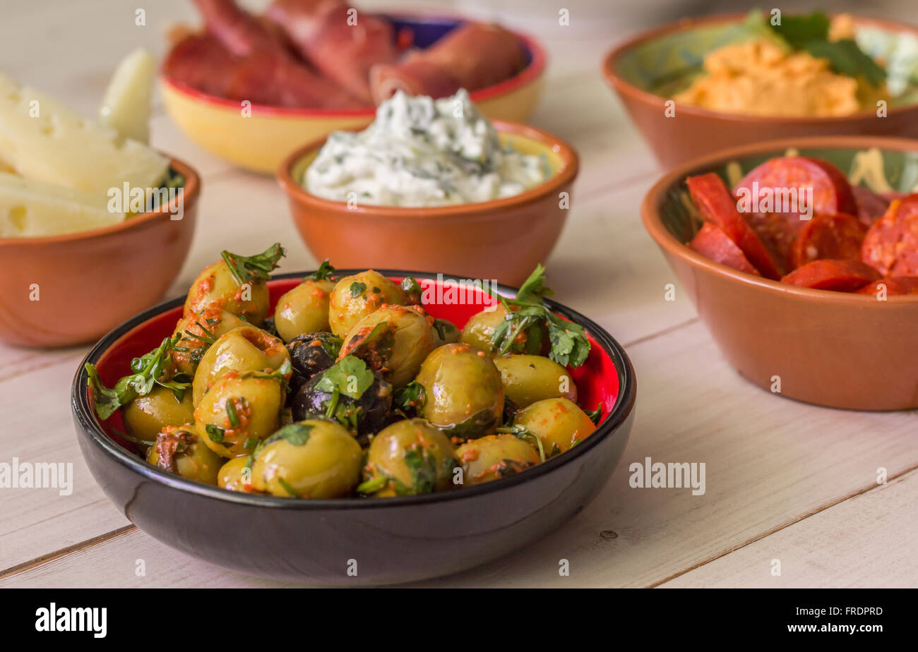 Tapas, aceitunas verdes, chorizo, queso manchego, tzatziki y el jamón en una tabla blanca Foto de stock