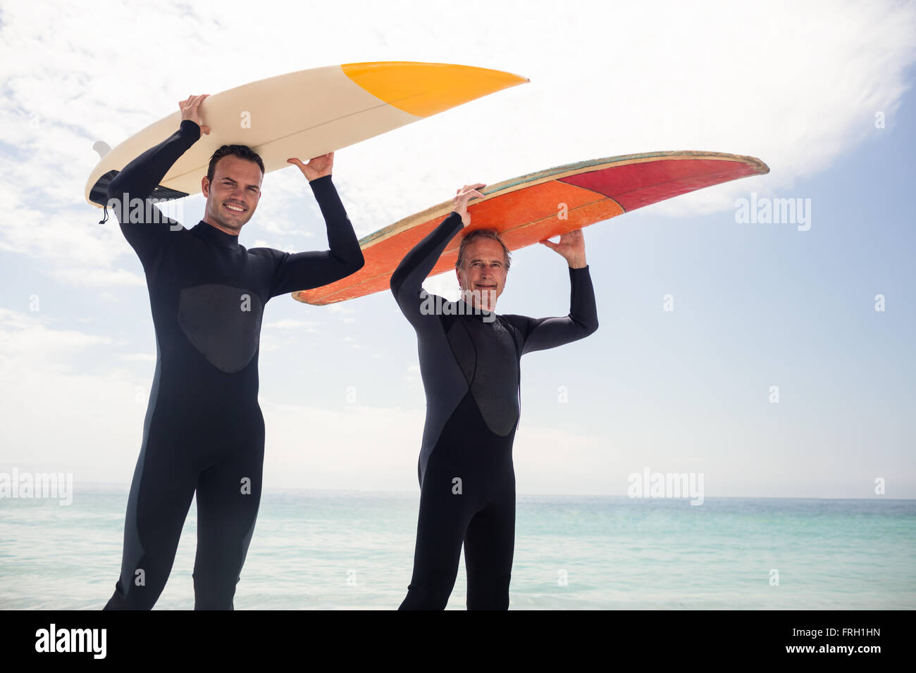 Retrato de padre e hijo feliz llevando una tabla de surf sobre su cabeza Foto de stock