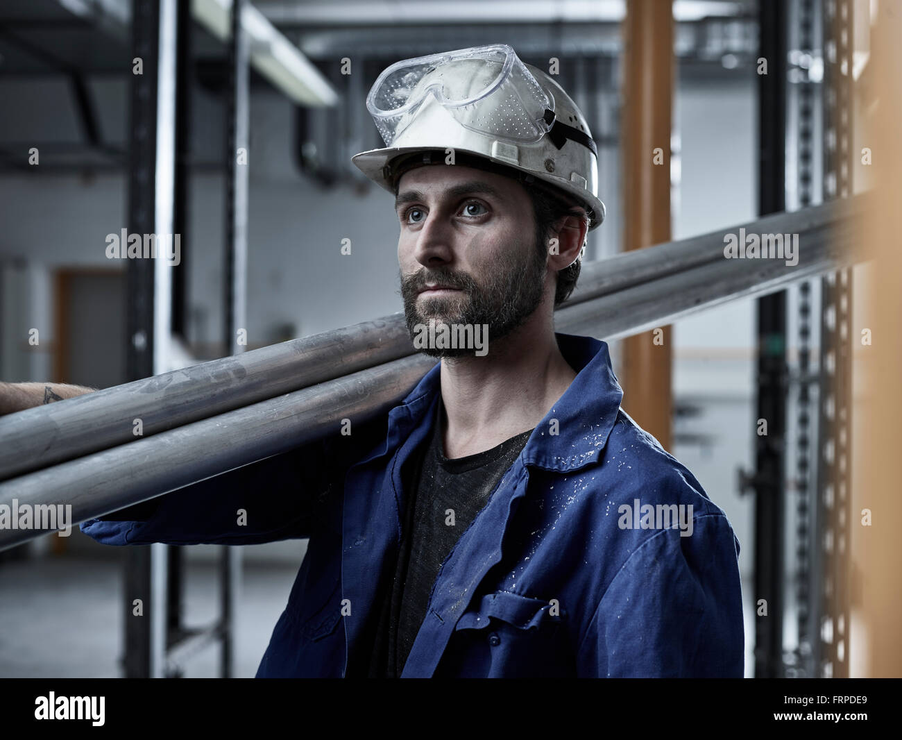Trabajador mecánico, con cascos y gafas de seguridad llevar tubos en su hombro, Austria Foto de stock
