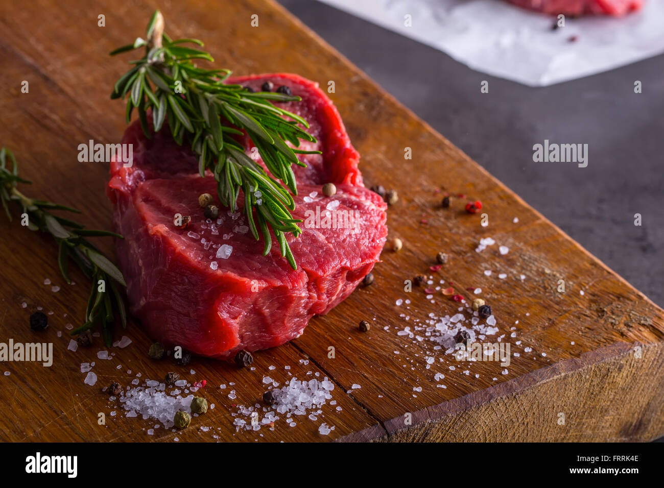 El bistec. Filete de carne cruda. Filete de carne de solomillo cruda fresca cortada en rodajas o todo listo para la barbacoa o parrilla. Hierba - Romero decoración. Foto de stock