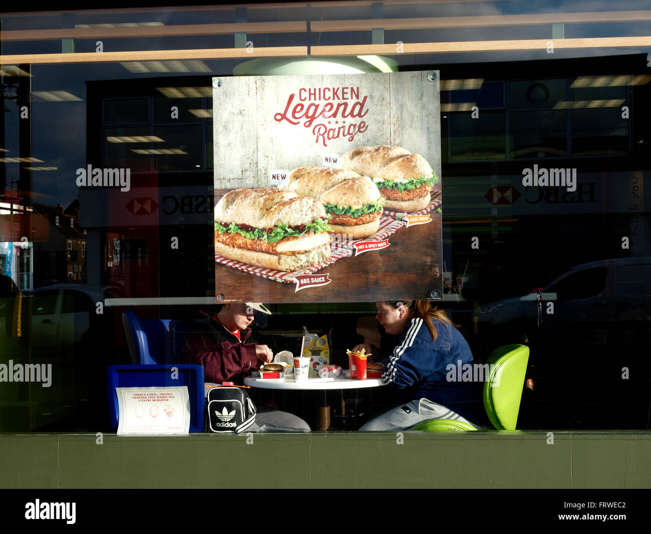 Pareja de jóvenes adultos en el asiento de ventana de un restaurante McDonald's, Havant, Hants, Reino Unido Foto de stock