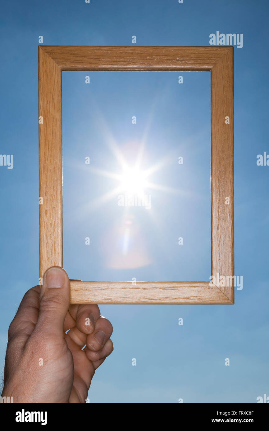 Un hombre mano un marco de imagen para el cielo parece haber capturado el sol en un cielo azul. Foto de stock