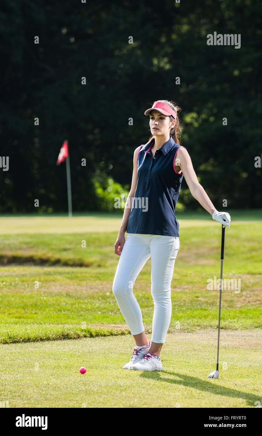 de una hermosa mujer mirando el verde del campo de golf. Ella está esperando delante de su bola rosa, sosteniendo su club en conjunto de ropa deportiva y una gorra