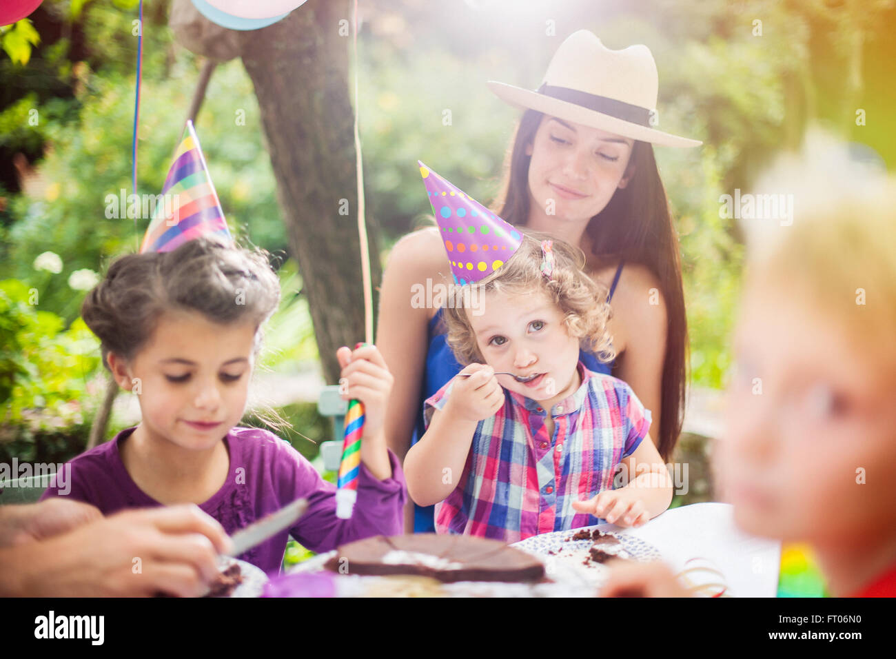 Garden Party familia compartiendo la torta de cumpleaños. El niño de 3 años  está disfrutando de su obra, el jardín está decorado con globos y los  colores son brillantes Fotografía de stock 