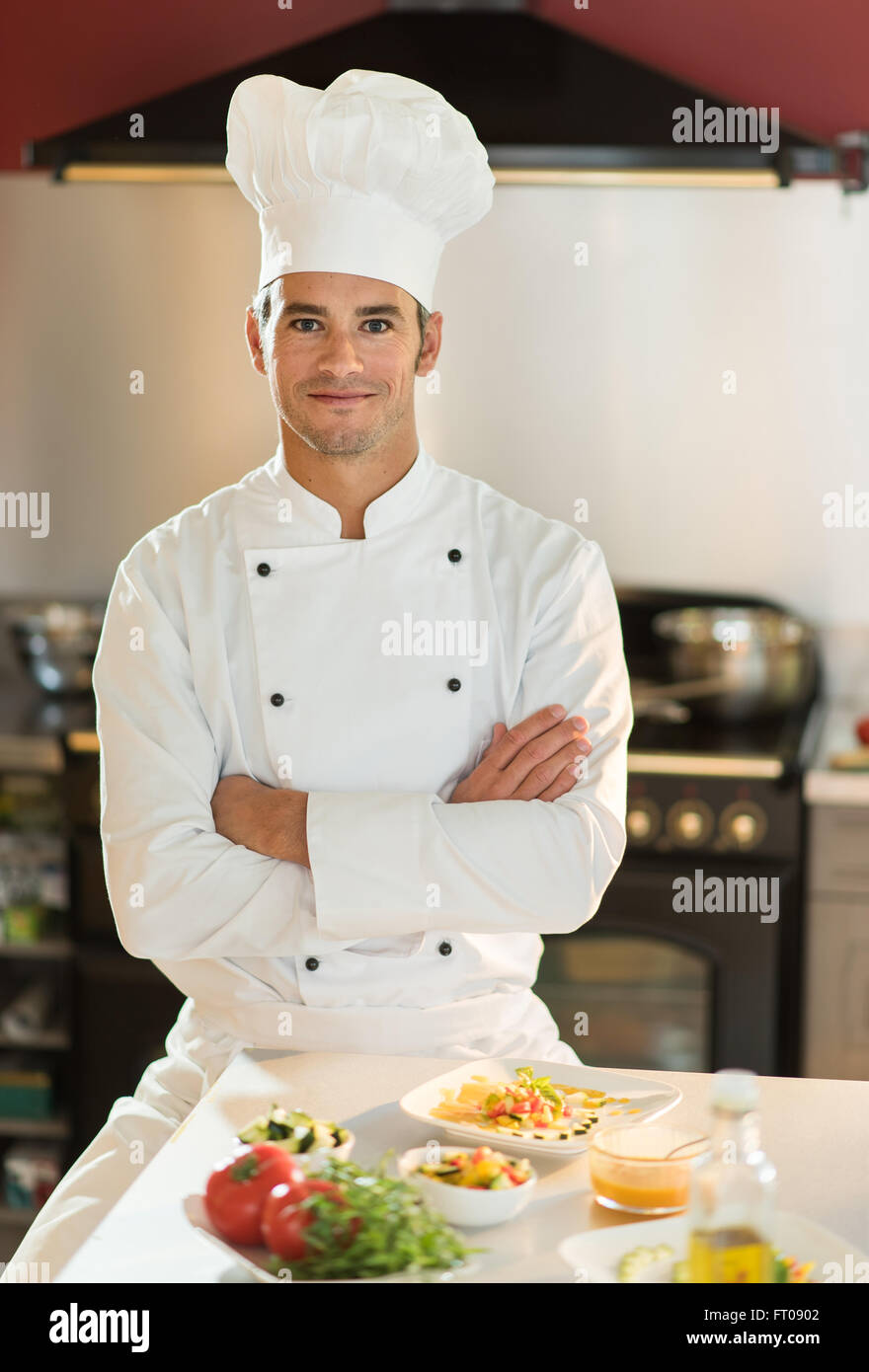 https://c8.alamy.com/compes/ft0902/retrato-de-un-hombre-chef-el-esta-mirando-a-la-camara-con-confianza-frente-a-una-mesa-de-cocina-con-platos-coloridos-el-esta-vistiendo-ropa-blanca-y-un-sombrero-de-chef-otra-mujer-chef-de-cocina-esta-detras-de-el-ft0902.jpg