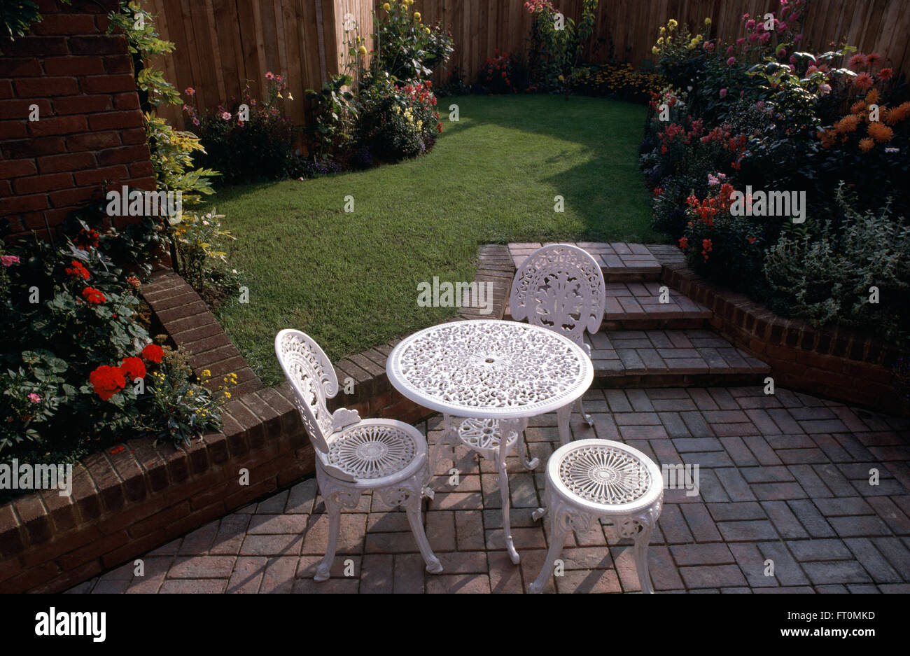 Sillas de hierro forjado blanco en un patio pavimentado en un jardín recién hechas con ladrillo sube un pequeño césped Foto de stock