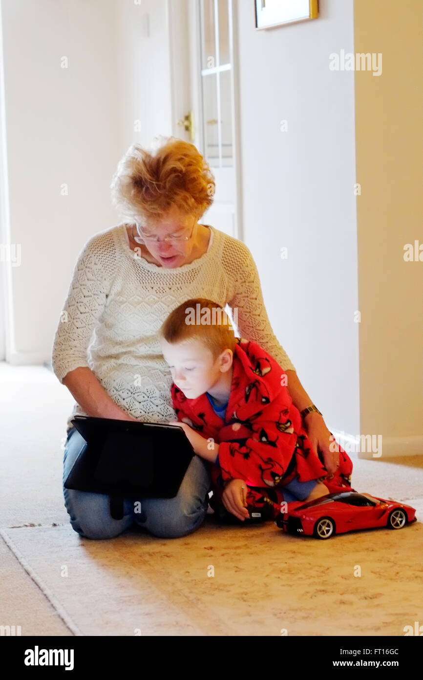 Una abuela con su nieto en ambos comparten un ipad o tablet mientras abrazados juntos. están iluminadas por la pantalla del dispositivo Foto de stock