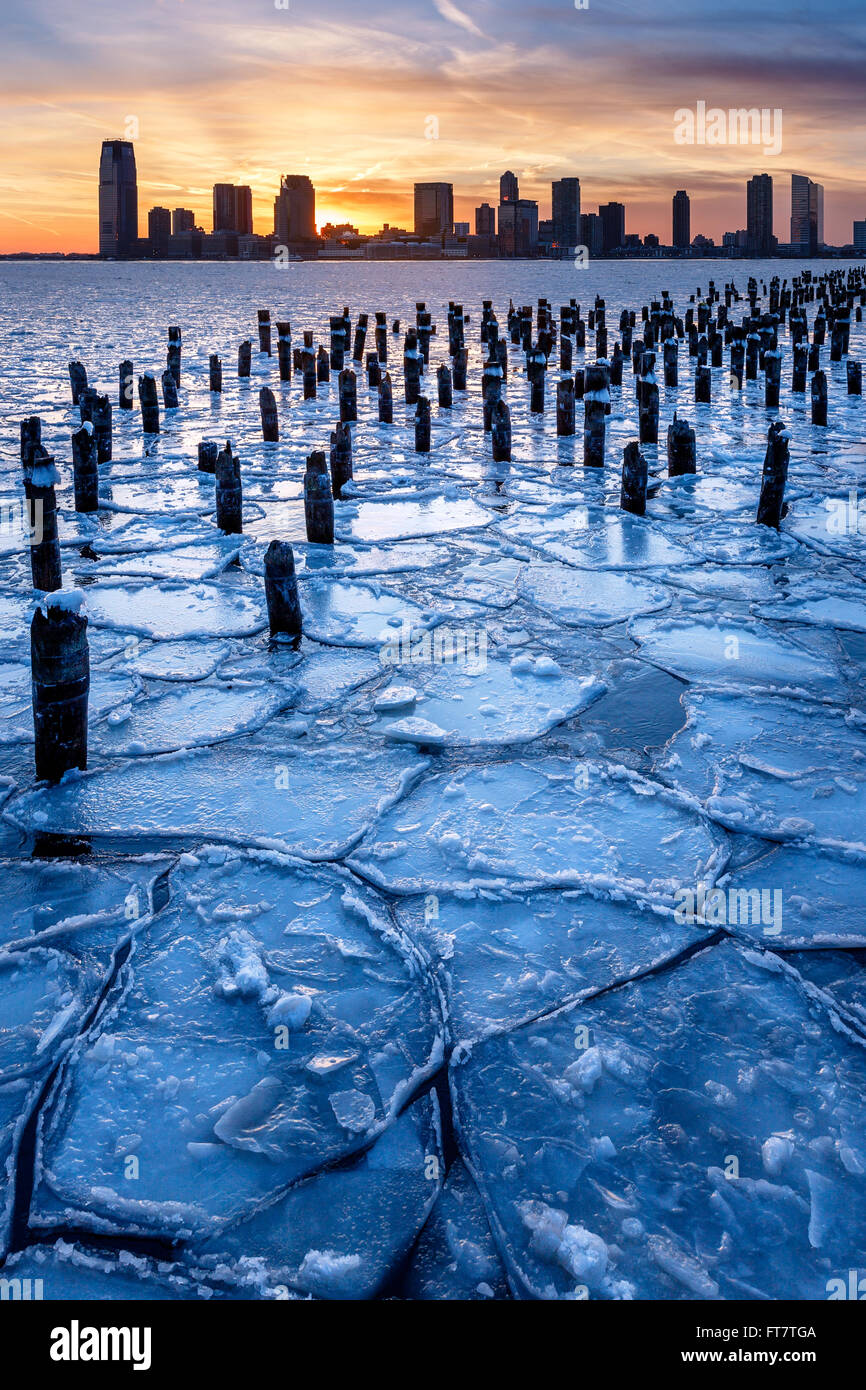 Horizonte de invierno del Río Hudson congelado con pilotes de madera vieja al atardecer con el centro de la ciudad de Jersey rascacielos Foto de stock