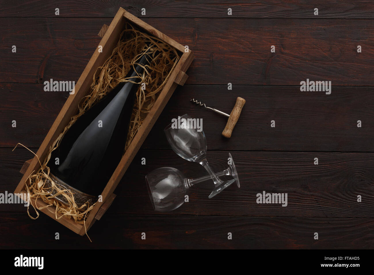 Botella de vino tinto en caja de madera llena de paja junto a vaciar con gafas sacacorchos sobre mesa de madera. Lay, plana por encima de vi Foto de stock