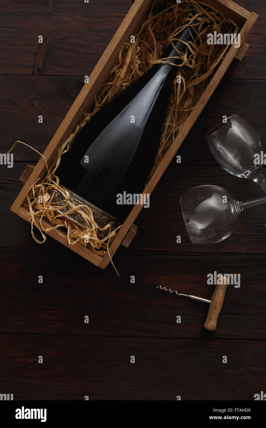 Botella de vino tinto en caja de madera llena de paja junto a vaciar con gafas sacacorchos sobre mesa de madera. Lay, plana por encima de vi Foto de stock