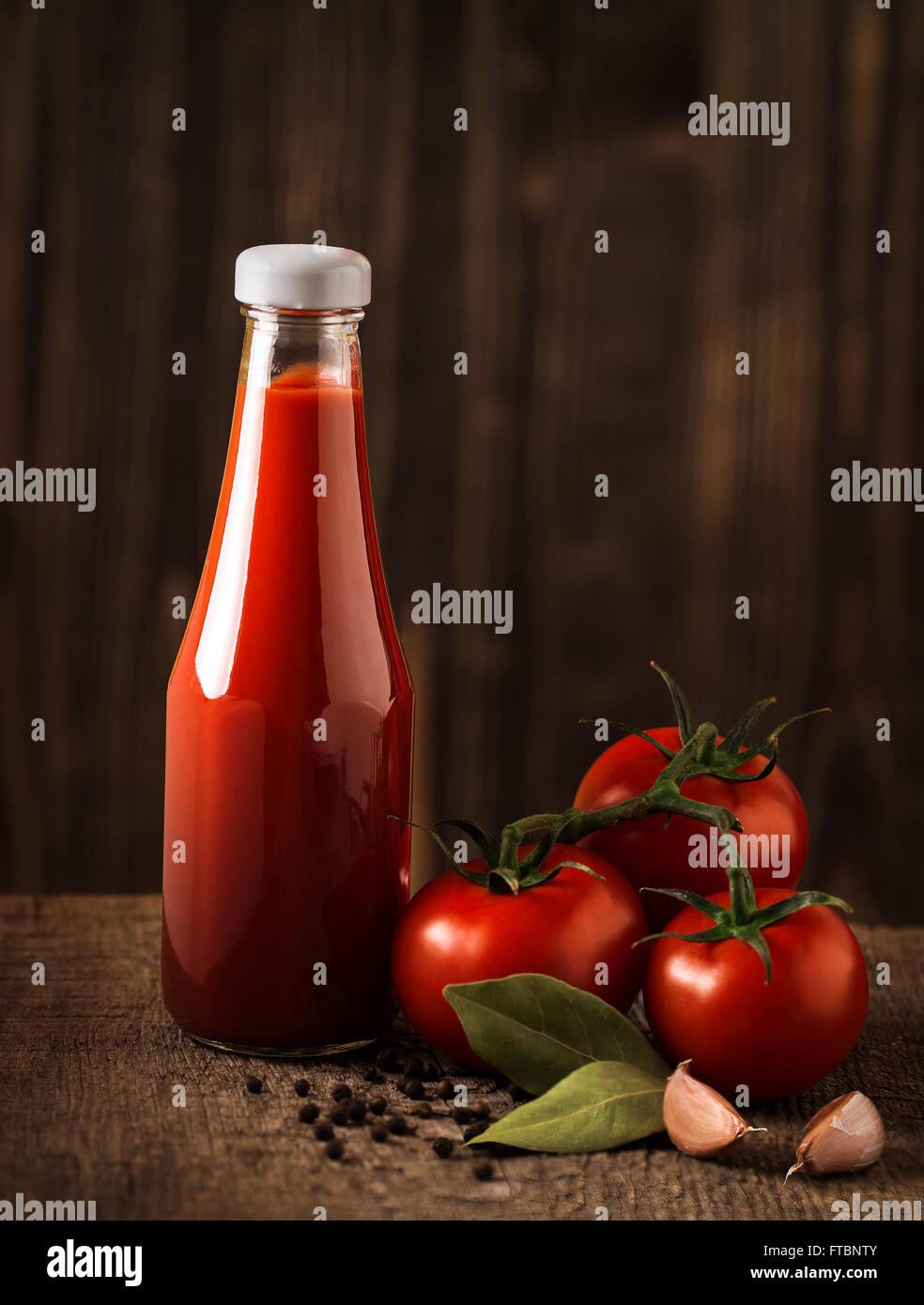Still life oscuro con salsa de tomate y los ingredientes sobre la madera en bruto Foto de stock