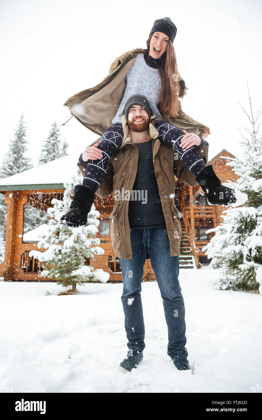 Hermosa pareja joven divirtiéndose cerca de la cabaña de troncos en invierno Foto de stock