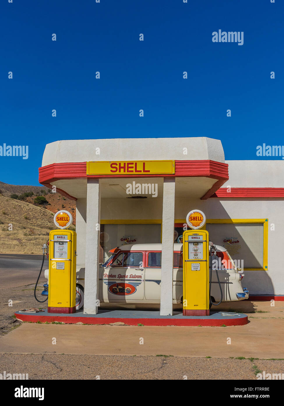 Clásica 1950 de la gasolinera Shell, pintada de amarillo y rojo en los colores del Shell y con una camioneta Ford 1952 estacionado en frente. Foto de stock