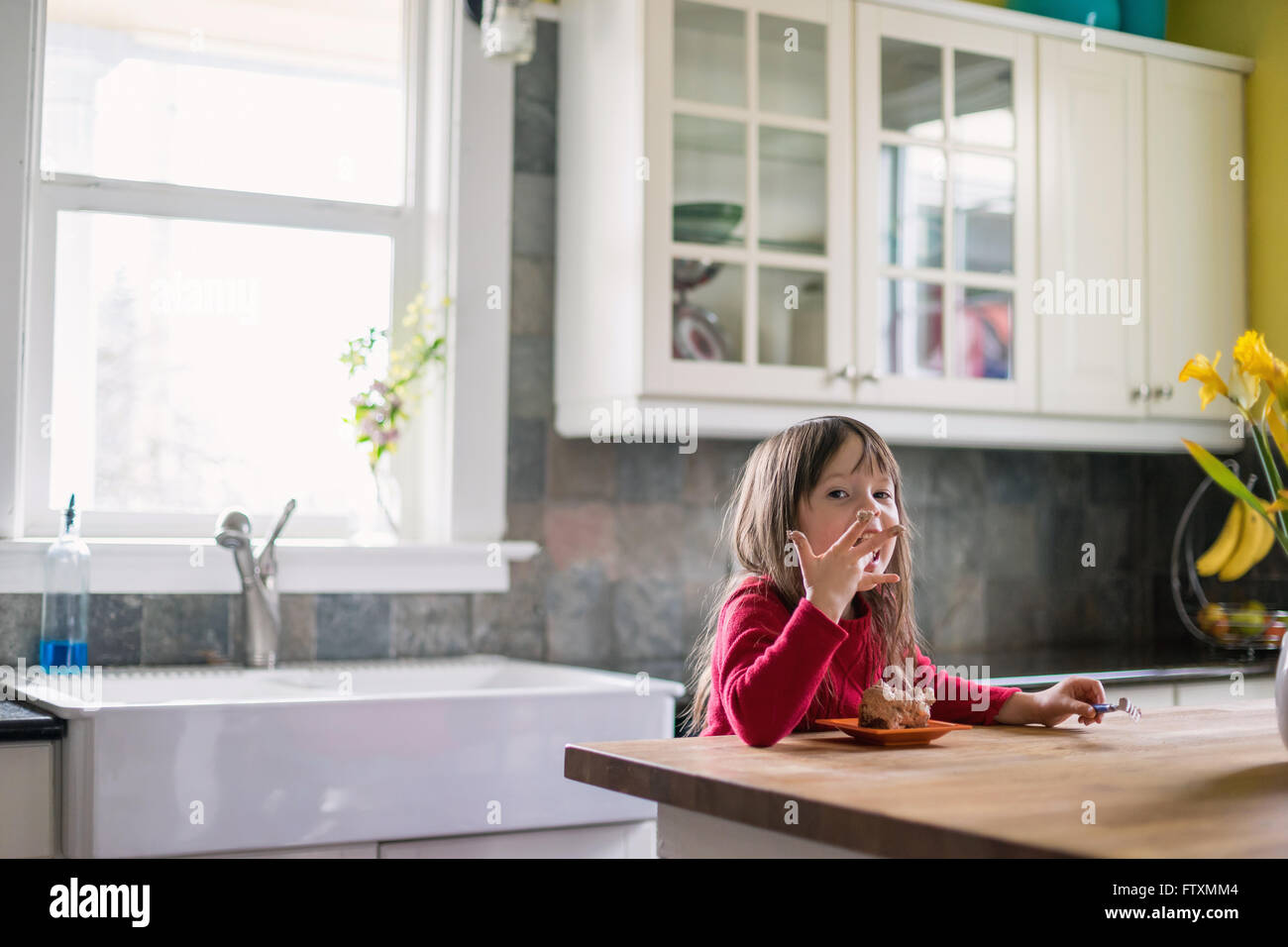 Chica sentada en la cocina comiendo postres de chocolate y lamer los dedos Foto de stock