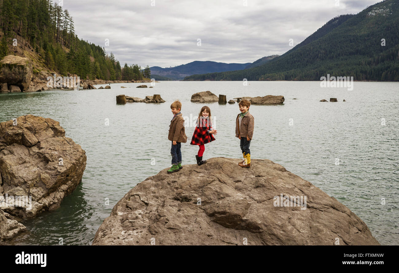 Tres niños de pie sobre una roca riendo en un valle del río Foto de stock