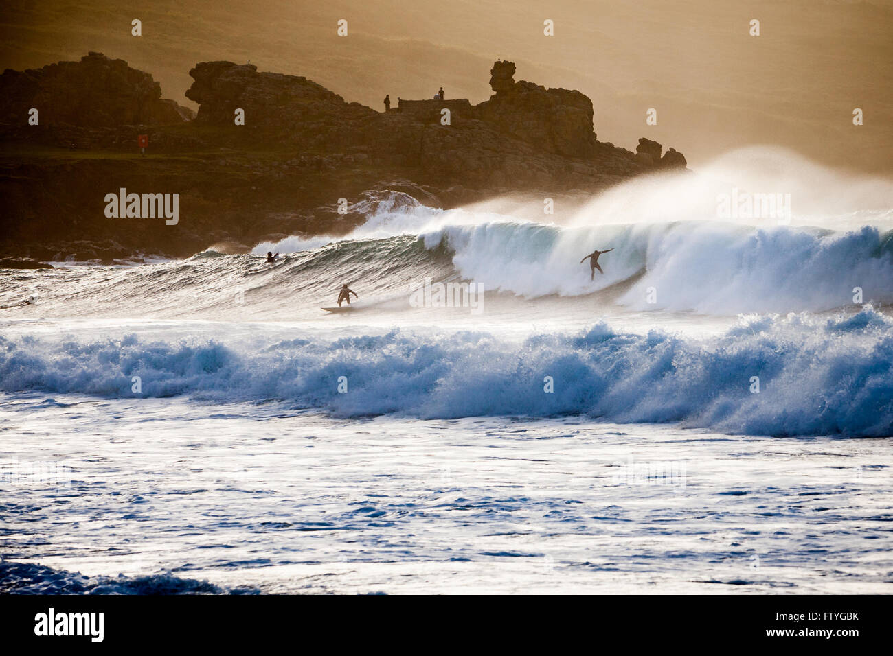 Siluetas de surfistas montando olas grandes en Porthmeor Beach en St Ives, Cornwall. Dividir el tratamiento de color de tono. Foto de stock