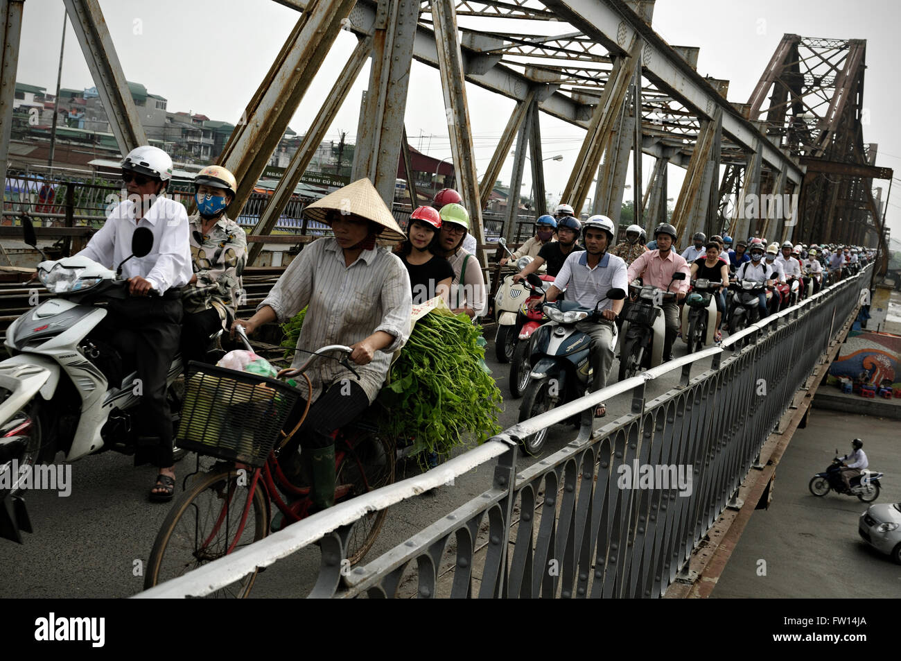 Mujer en bicicleta y otras muchas personas con motocicletas en Long bien puente durante la hora punta en Hanoi, Vietnam Foto de stock