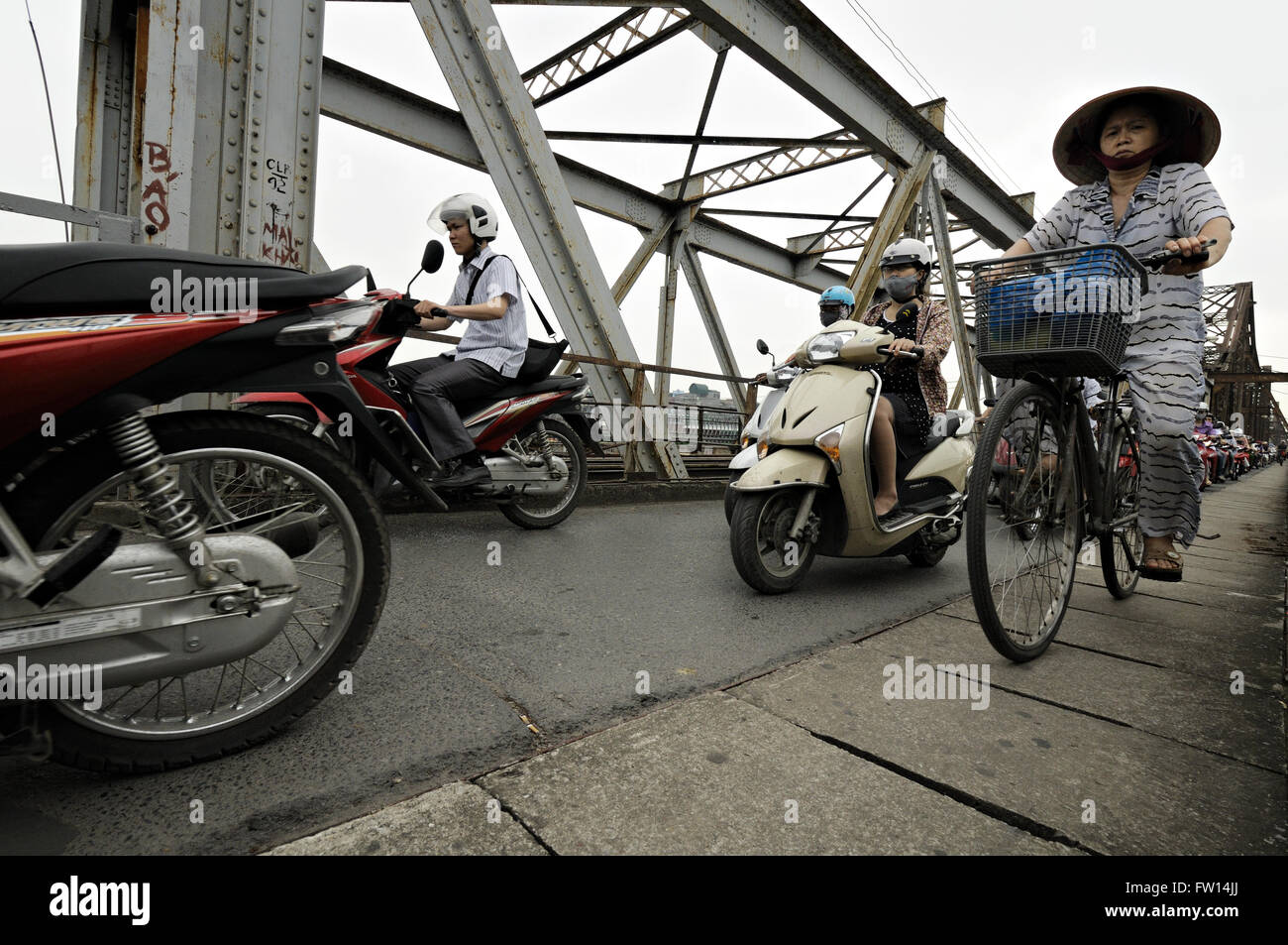 Mujer con sombrero cónico típico montar en bicicleta y otras muchas personas con motocicletas en Long bien puente en Hanoi, Vietnam Foto de stock