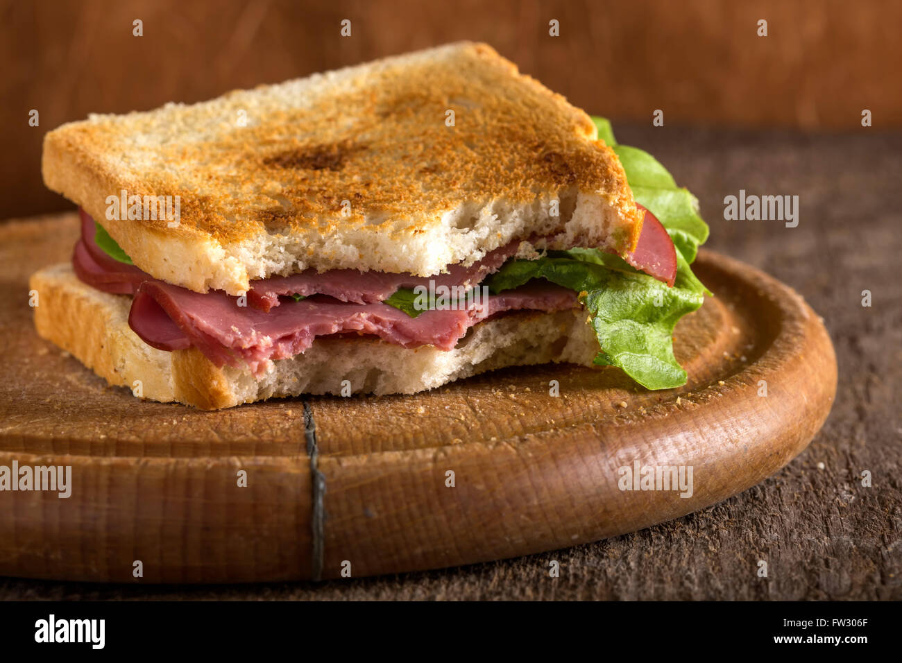 Mordido carne pastrami sandwich con lechuga y tomate sobre fondo de madera Foto de stock