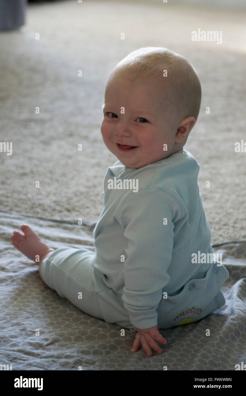 Un feliz 8º mes El bebé niño sonriendo, y sentada en el piso usando una luz azul romper. Foto de stock