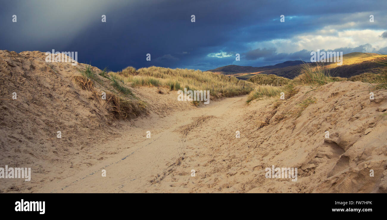 Fotografía de una ruta corriendo a través de dunas de arena con nubes de tormenta comienzan a formar por encima. Foto de stock