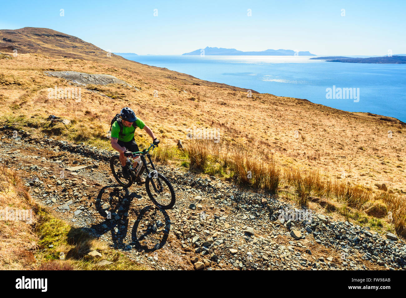 Ciclista de montaña descendente a Camasunary Isla de Skye Escocia con la isla de ron en el horizonte Foto de stock
