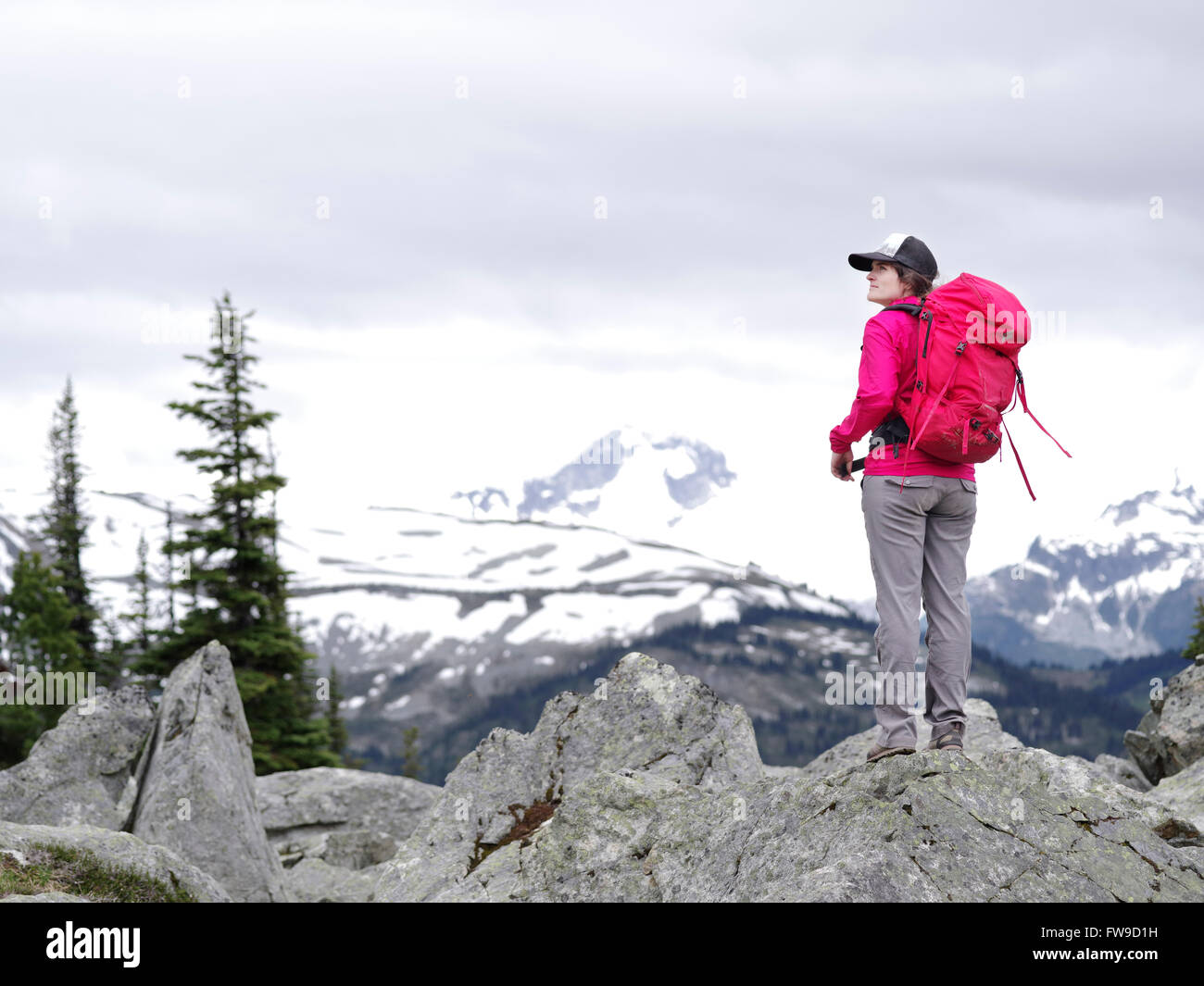 Joven mujer caucásica senderismo en Whistler Blackcomb trail de pie y mirando hacia Whistler Mountain Foto de stock