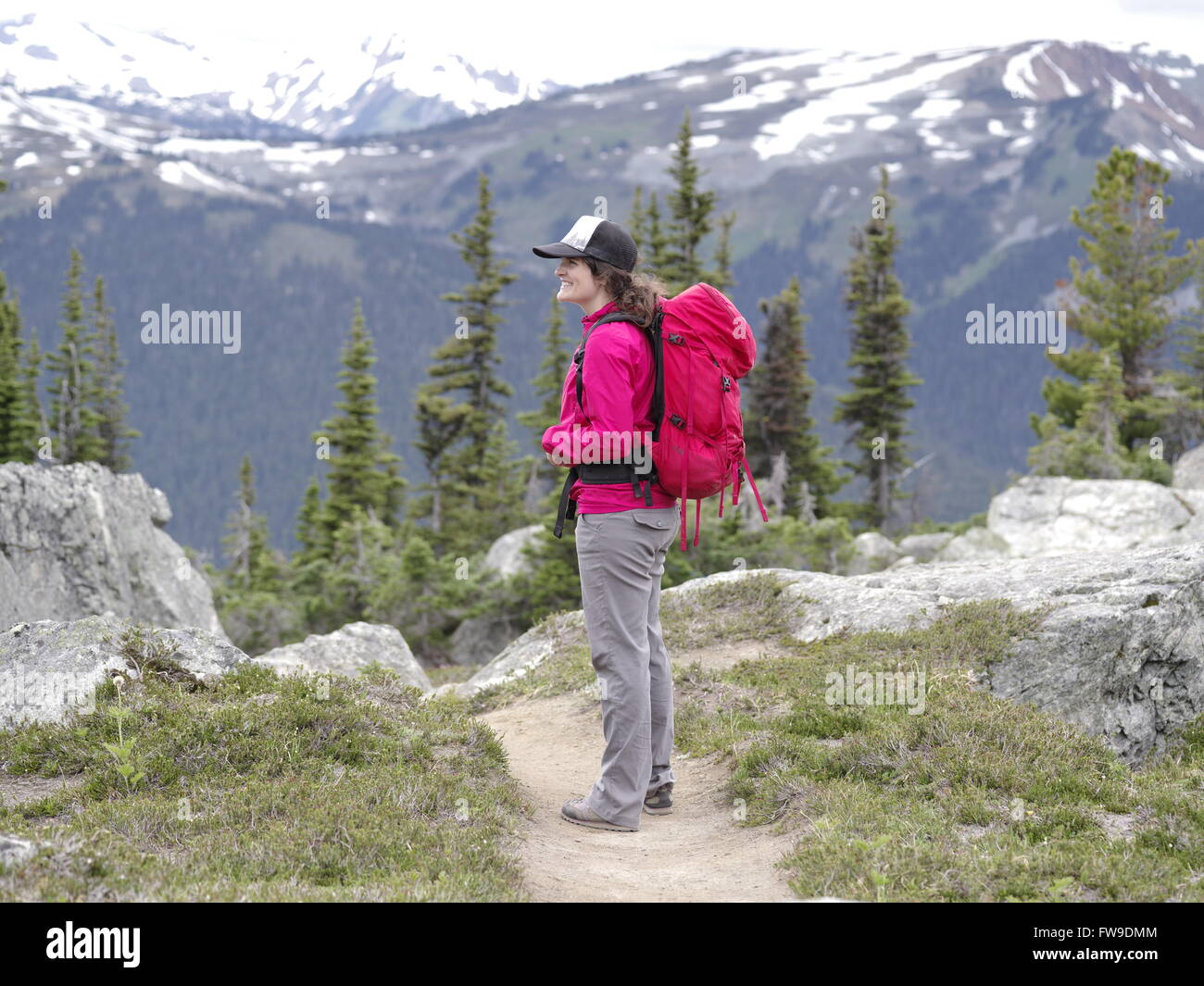 Joven mujer caucásica senderismo en Whistler Blackcomb trail de pie y mirando hacia Whistler Mountain Foto de stock