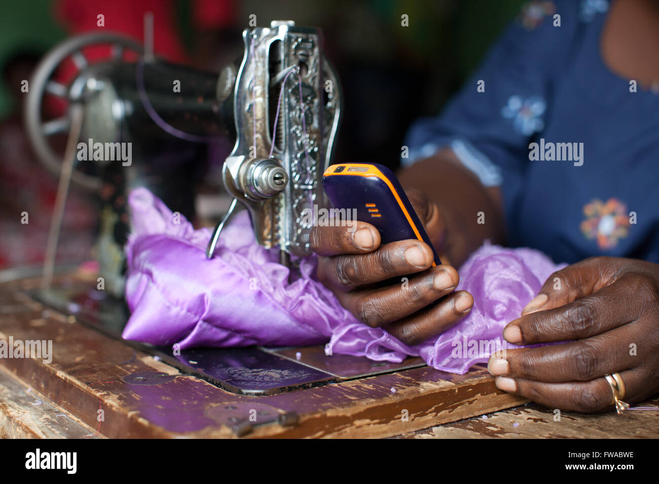 Una vestimenta femenina Maker usando una máquina de coser y un teléfono móvil, Nigeria, África Foto de stock