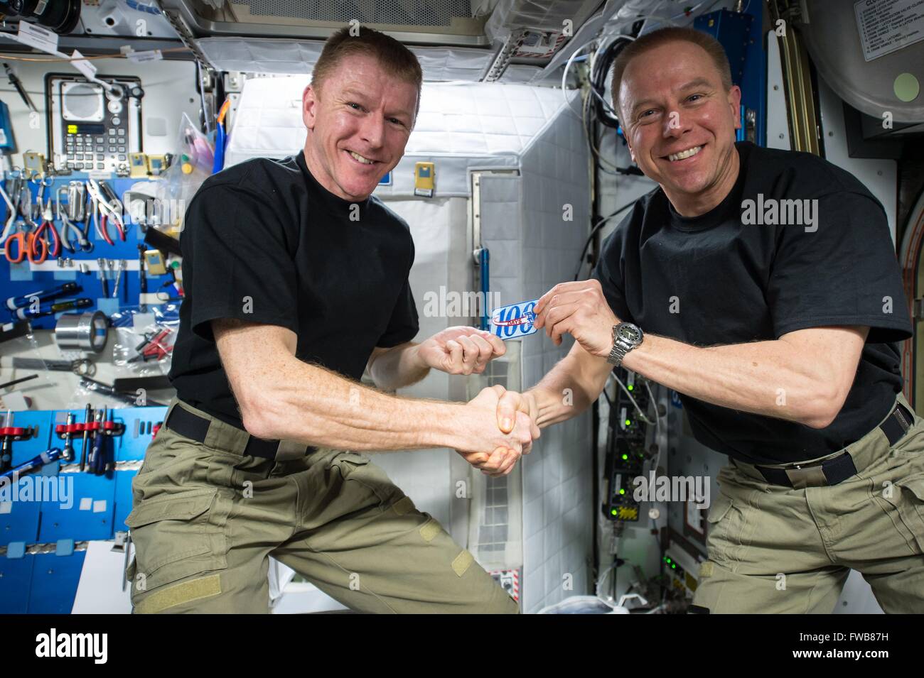 El astronauta estadounidense Tim Kopra, derecha, presenta el astronauta de la Agencia Espacial Europea Tim Peake con un parche para conmemorar su centésimo día en el espacio a bordo de la Estación Espacial Internacional el 24 de marzo de 2016 en la órbita de la tierra. Foto de stock