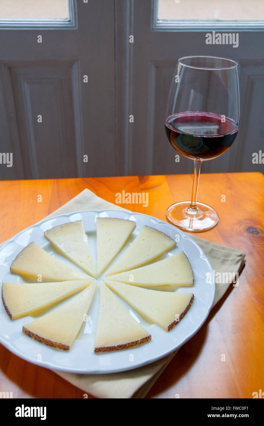 El queso manchego sirviendo y copa de vino tinto. España. Foto de stock